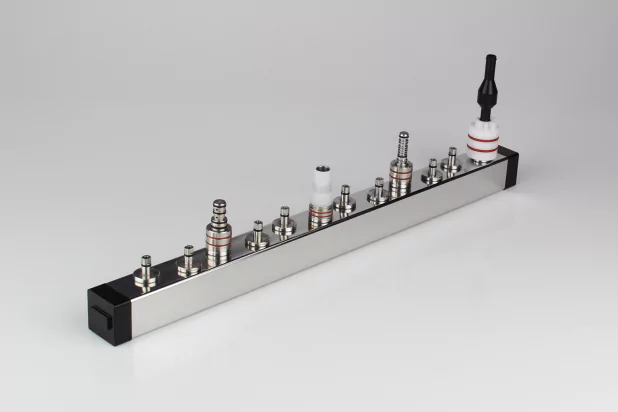 Metallischer Verteilerblock mit mehreren Anschlüssen und roten Dichtungselementen, ideal für technische Anwendungen und industrielle Steuerungssysteme.